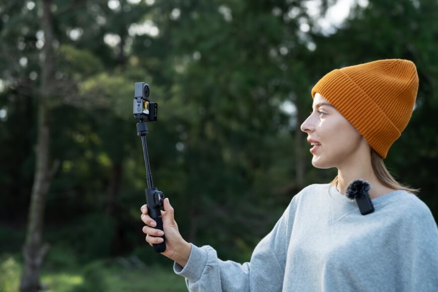 A woman holds a DJI Action 2 camera on a selfiestick