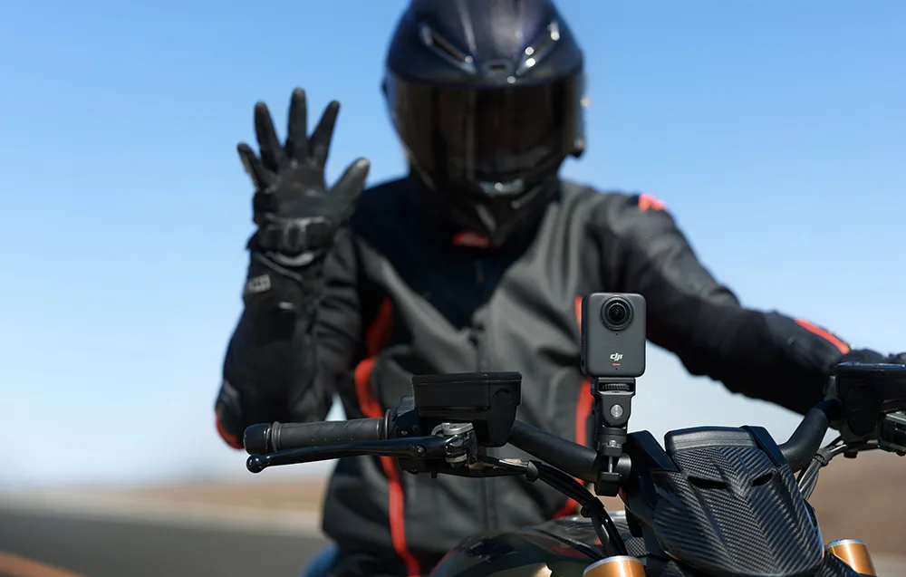 machający motocyklista z kamerą sportową przymocowaną do kierownicy
