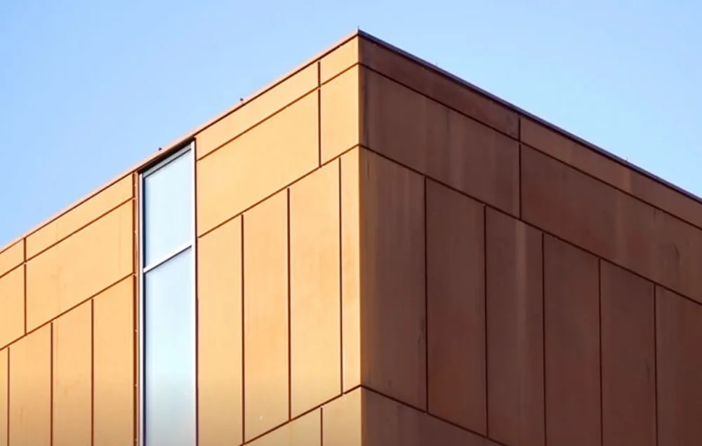 Corner of a modern building with orange facade and vertical window against the sky