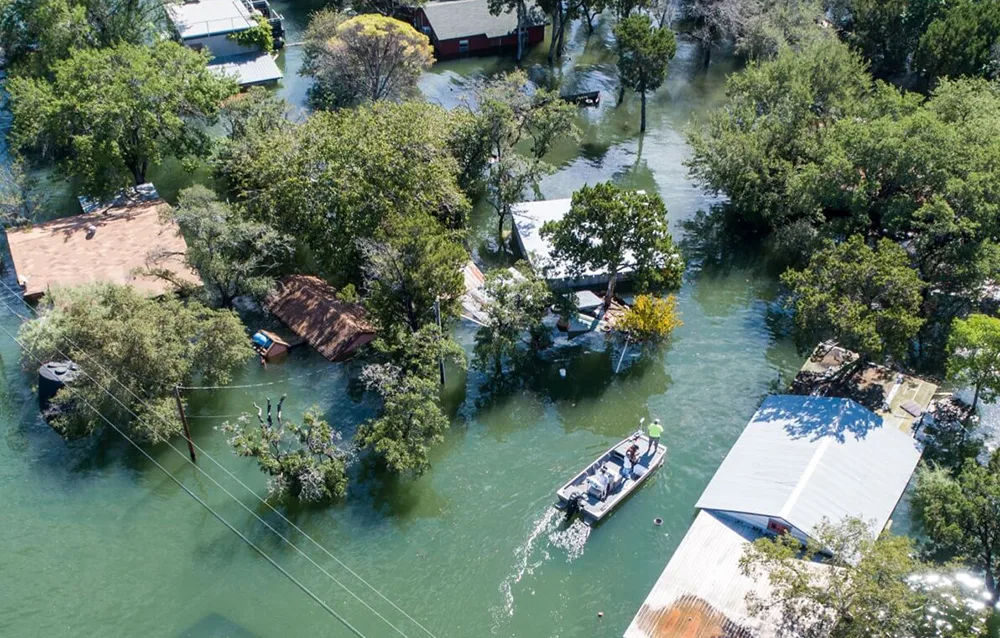 Flooded residential area with houses, trees, and a boat carrying people