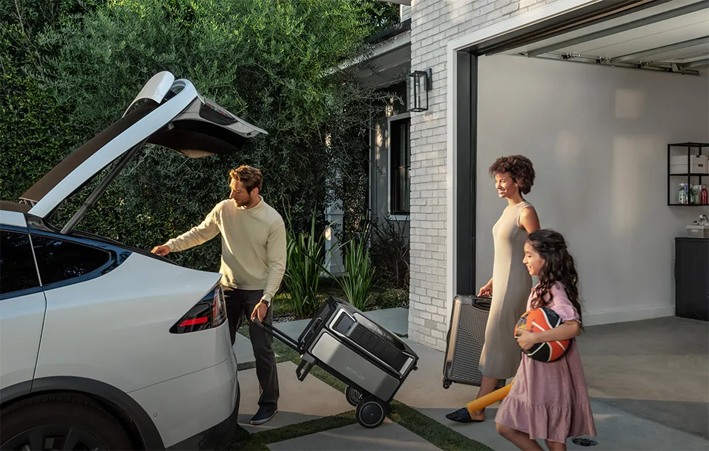 Family loading an EcoFlow portable power station into the trunk of a white car outside a garage