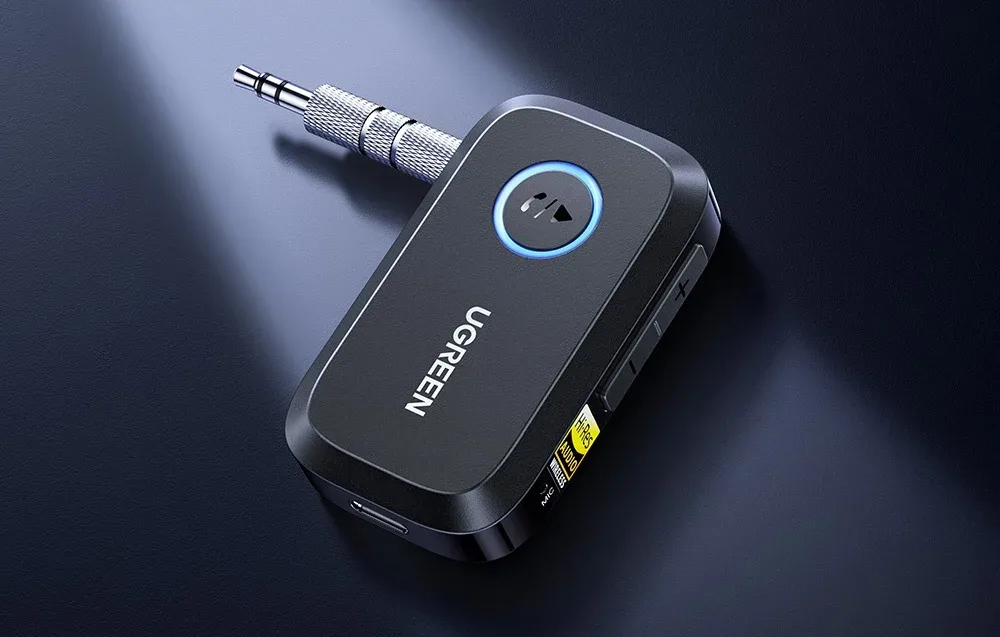 Czarny adapter Bluetooth UGREEN z podświetlanym przyciskiem i złączem jack na ciemnym tle