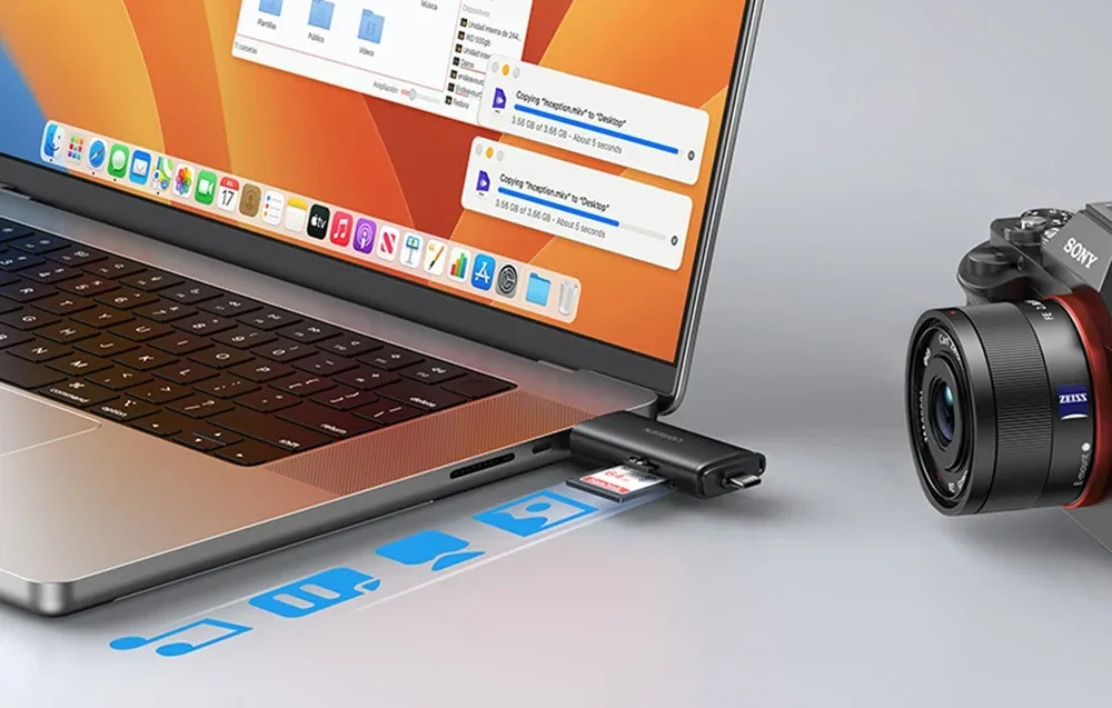 Laptop z pomarańczowym tapetą podłączony do czarnego adaptera UGREEN obok aparatu fotograficznego na biurku