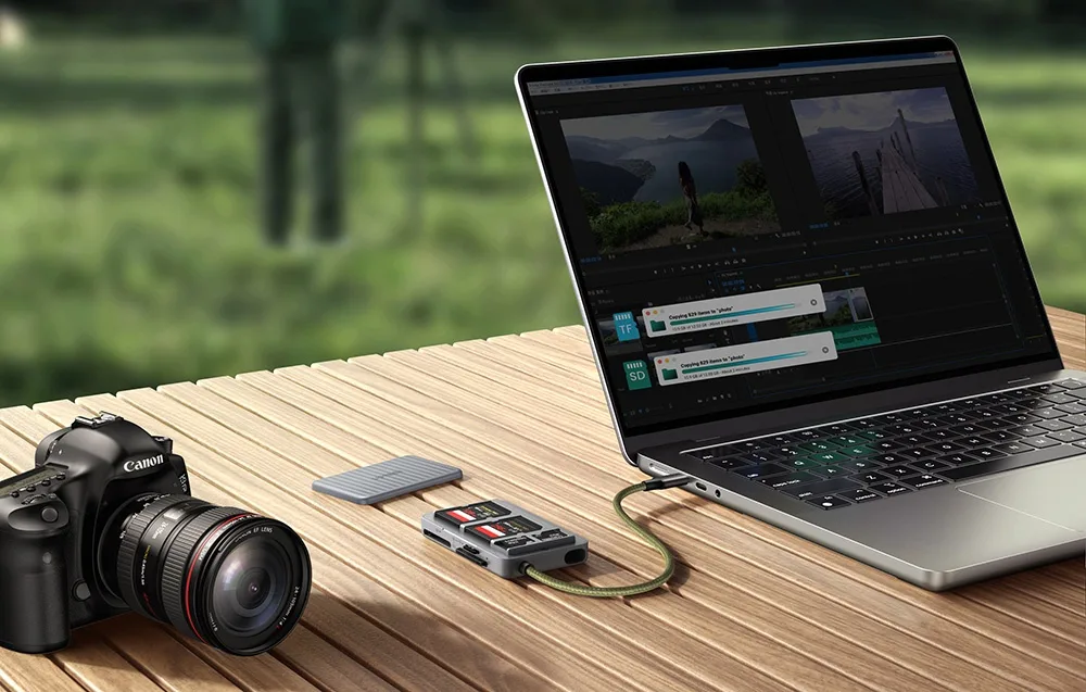 Laptop na stole z otwartym programem do montażu wideo jest podłączony do czytnika kart obok aparatu fotograficznego