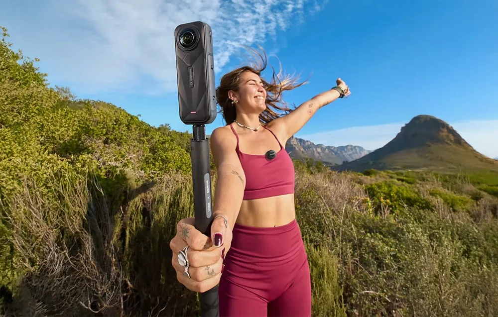 Жінка у рожевому спортивному одязі тримає камеру Insta360 X5, а на її футболці закріплений передавач Insta360 Mic Air