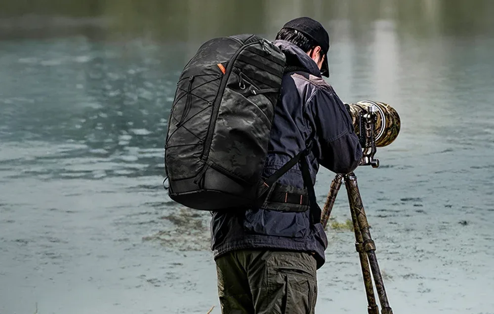Photographer by the water carrying the PGYTECH OnePro ST backpack and shooting with a camera on a tripod