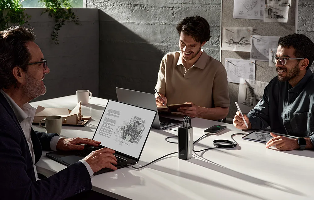 Three men sitting at a table using laptops and a tablet with the EcoFlow power bank placed in the center.