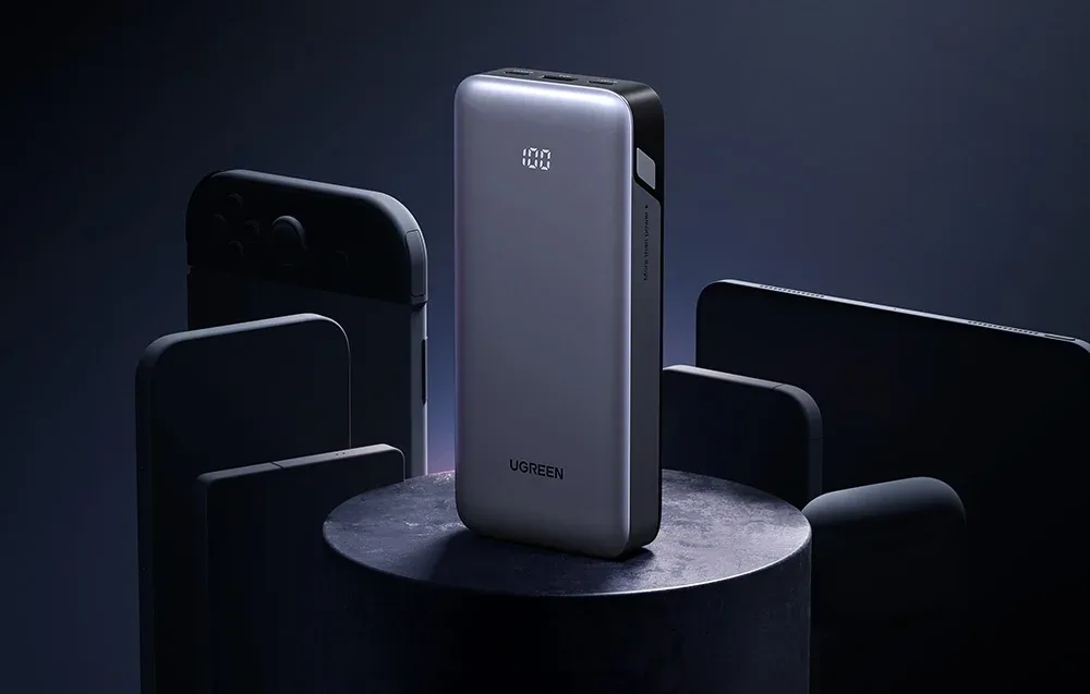 Ugreen power bank standing vertically on a cylindrical pedestal surrounded by dark smartphones