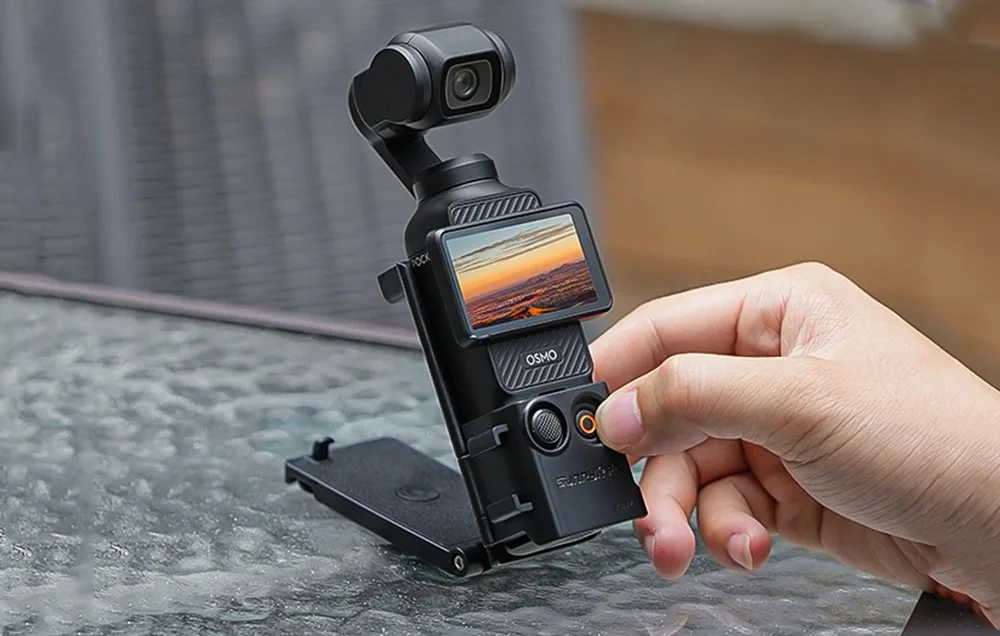 Kamera DJI Pocket złożona na stole z rozłożoną podpórką i ręką sięgającą do przycisku