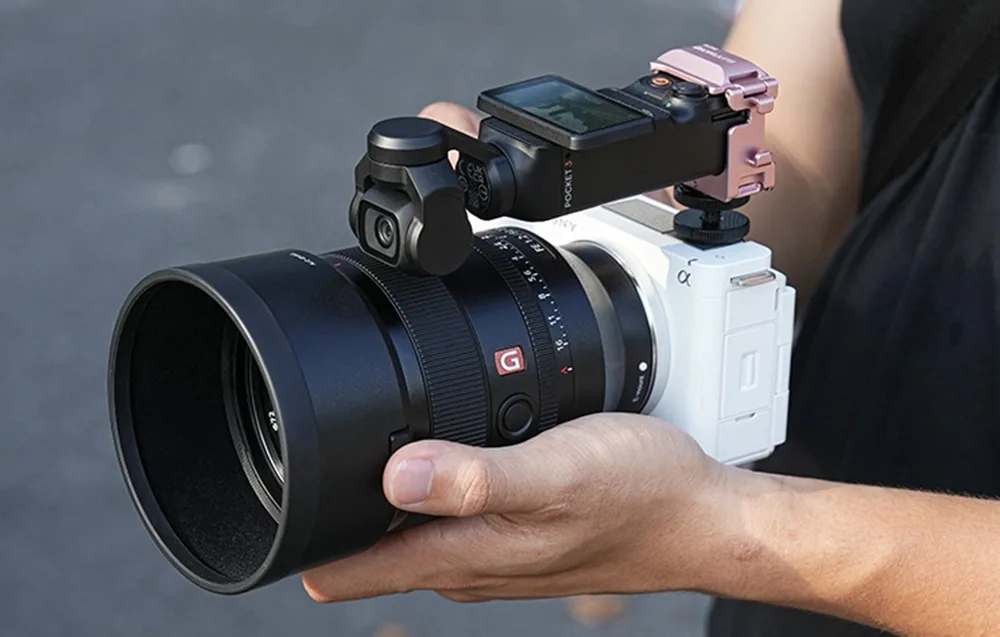 Kamera DJI Pocket w różowym uchwycie zamontowana na górze aparatu Sony z dużym obiektywem, trzymanego w dłoniach