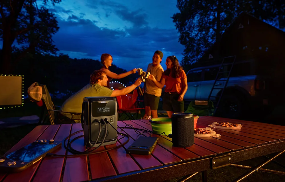 Group of people making a toast at a camping table with the EcoFlow TRAIL 300 DC and a speaker in the evening