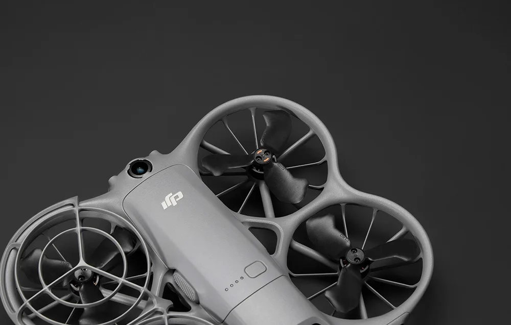 Szary dron DJI z czterema śmigłami osłoniętymi pierścieniami, widoczny z góry na czarnym tle