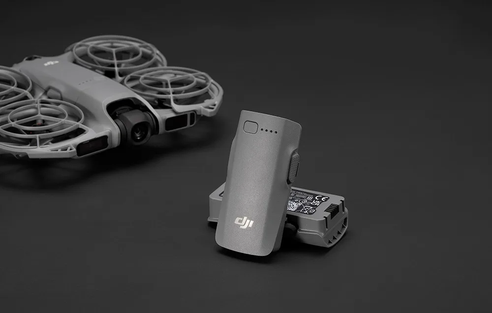 DJI Neo 2 intelligent battery standing in the foreground with a gray DJI drone in the background on a black backdrop