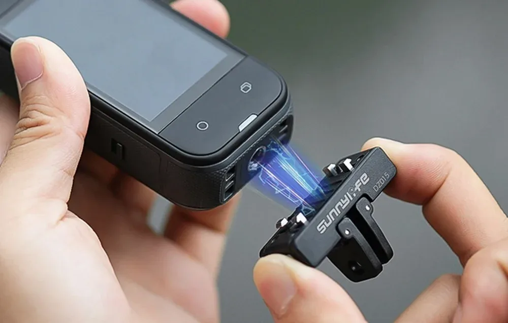 Zbliżenie na dłonie trzymające kamerę sportową i magnetyczny adapter Sunnylife podczas podłączania