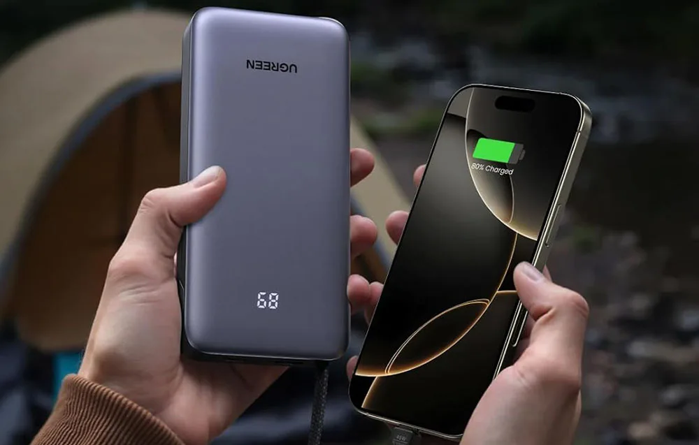 Hands holding a smartphone and gray UGREEN power bank with LED display.