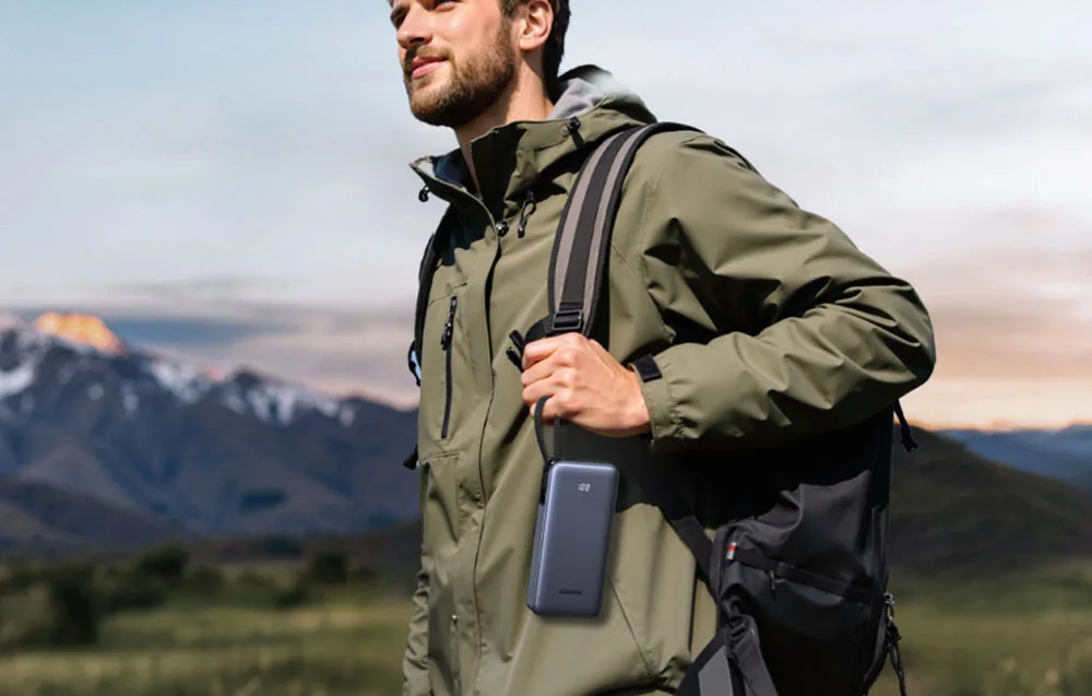 Man holding the gray UGREEN power bank outdoors with a mountain landscape in the background.