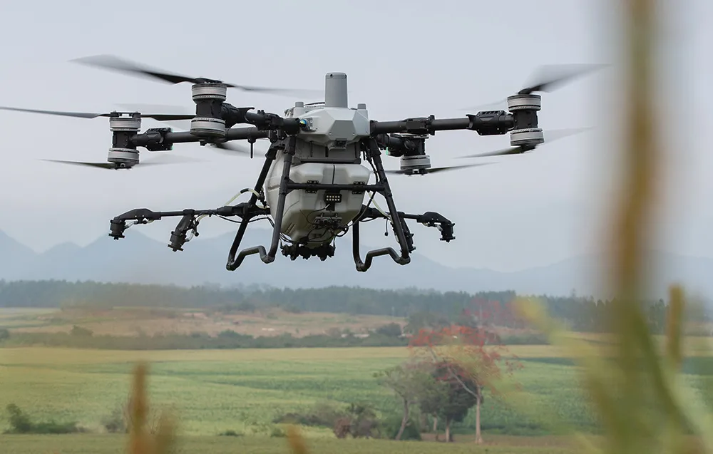 Dron rolniczy DJI Agras T25P na tle zielonego pola i pagórków