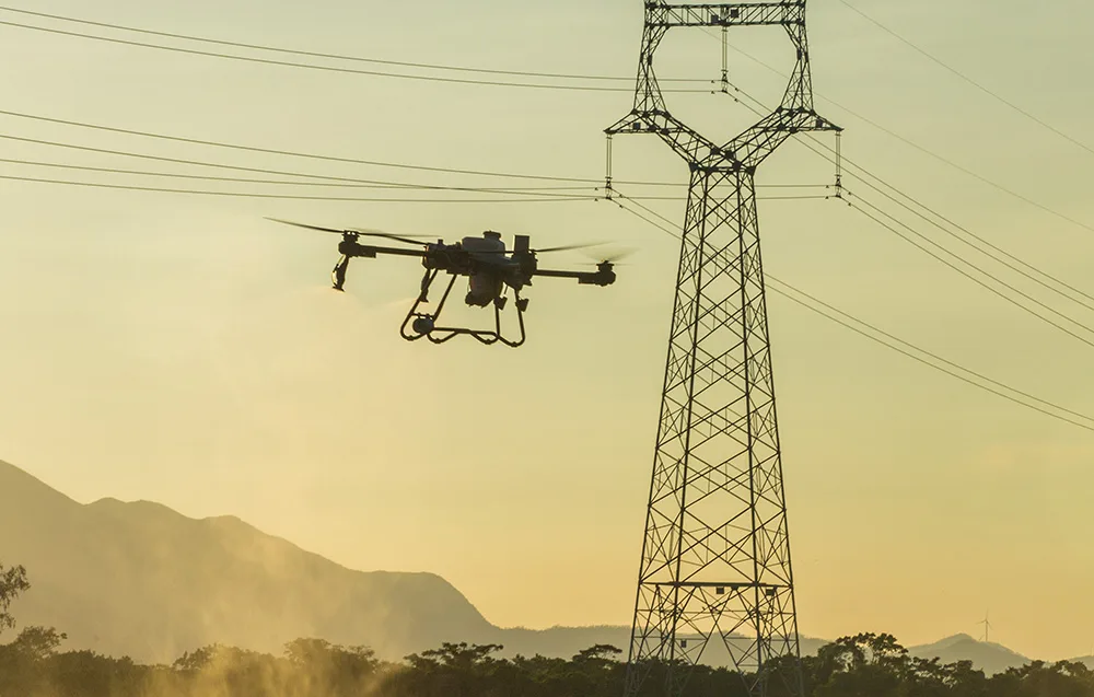 Dron rolniczy przelatujący obok linii energetycznych o zachodzie słońca