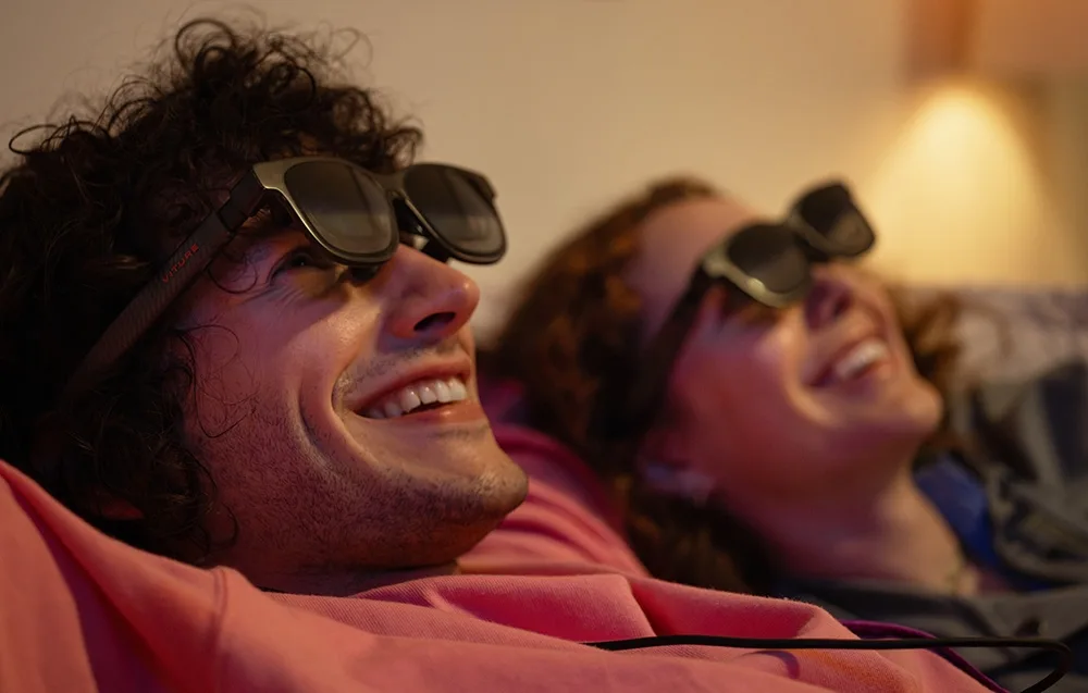 Woman and man wearing VITURE XR Luma Pro glasses laughing while lying down in a warmly lit room