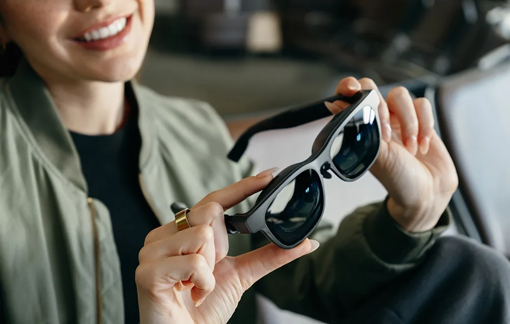 Smiling woman holding black VITURE XR Luma Pro extended reality glasses in her hands