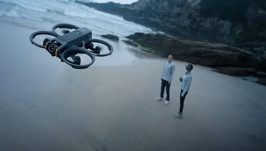Dron DJI Avata 2 unosi się nad plażą, a w tle stoją dwie osoby