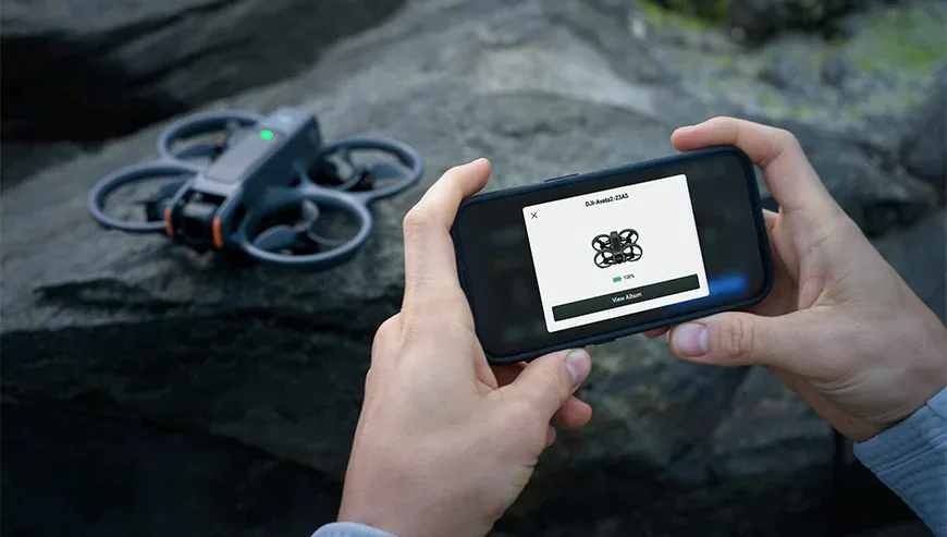 Osoba trzyma smartfon z aplikacją pokazującą połączenie z dronem DJI Avata 2, który leży obok na skale