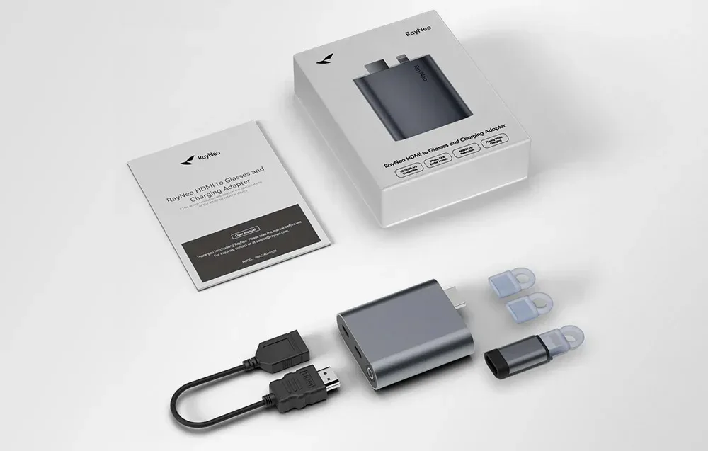 Zestaw RayNeo z adapterem, przejściówkami, kablem HDMI i instrukcją, ułożony obok opakowania na jasnym tle.