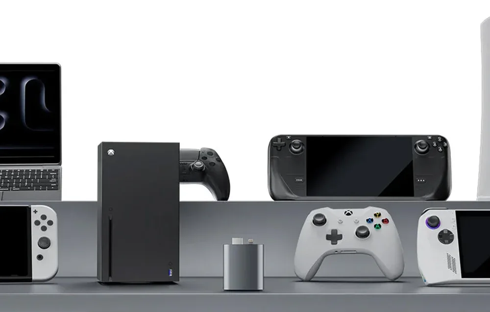 Adapter umieszczony na tle różnych urządzeń gamingowych i multimedialnych, w tym konsol, kontrolerów, laptopa i handheldów.