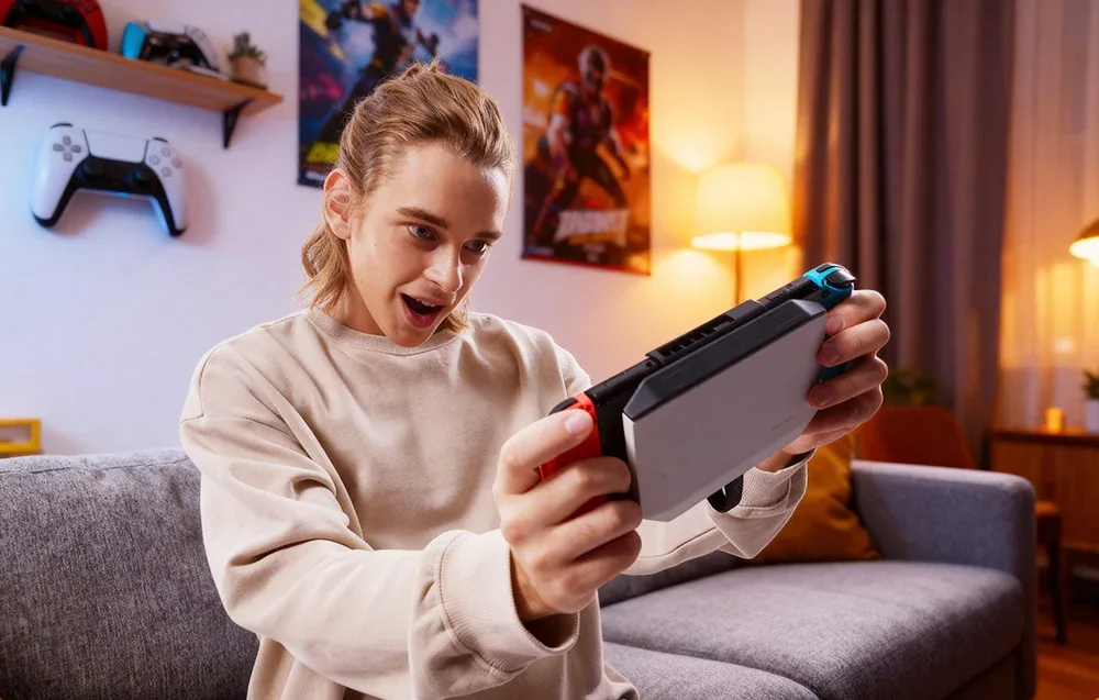 Kobieta trzymająca konsolę Nintendo Switch 2 z doczepioną mobilną stacją dokującą, uśmiechająca się i grająca w grę.