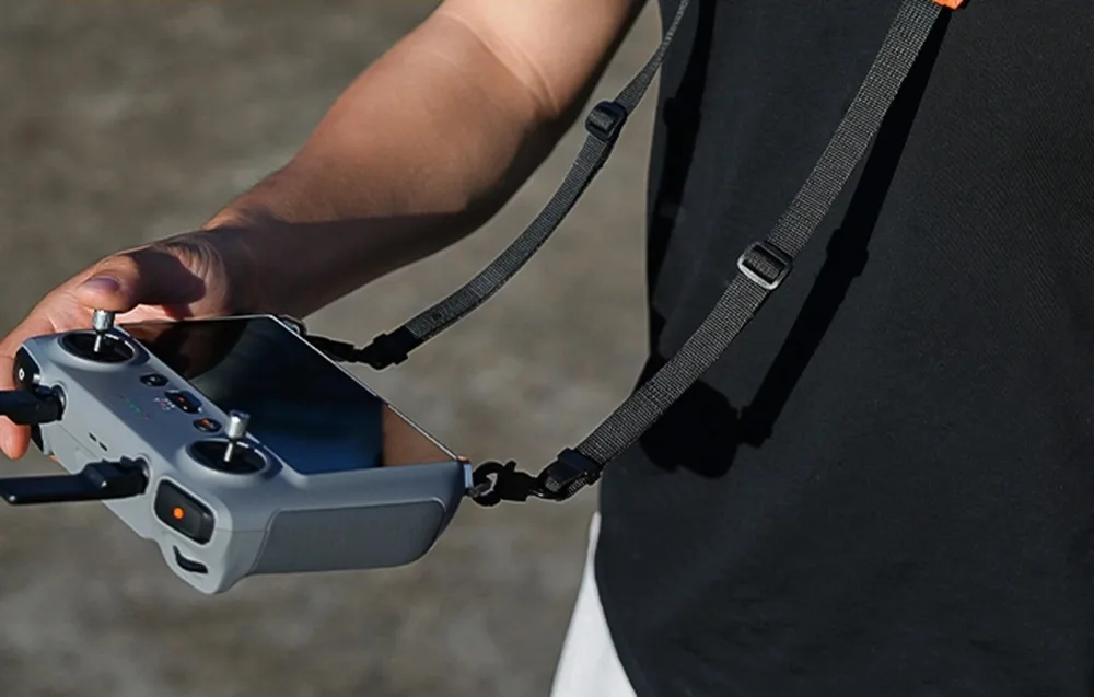 Drone controller suspended on a black Sunnylife neck strap during use