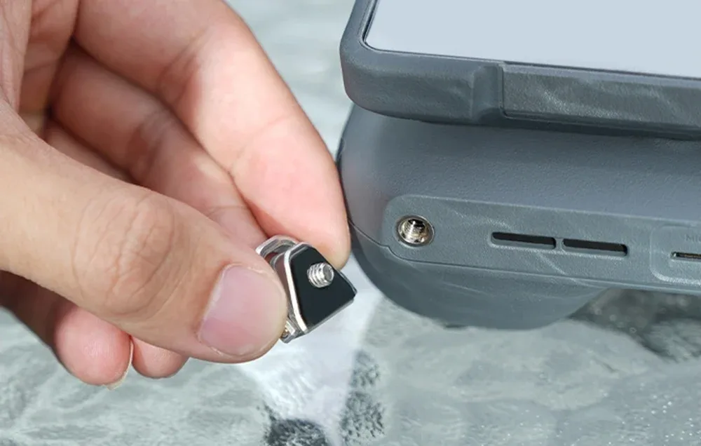 Hand holding a metal neck strap connector next to a gray drone controller