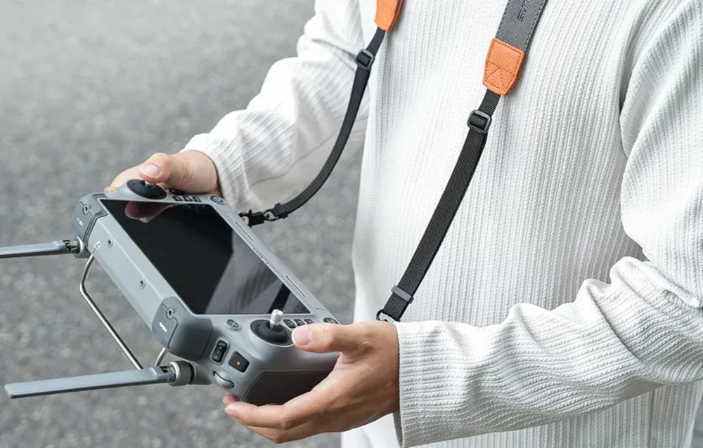 Person holding a drone controller with a Sunnylife neck strap featuring orange accents