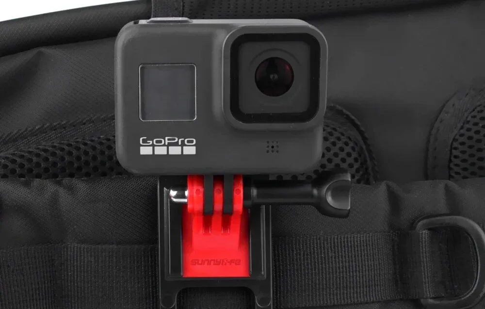Екшн-камера GoPro, закріплена в червоному кліпсі на чорній лямці рюкзака, вигляд спереду