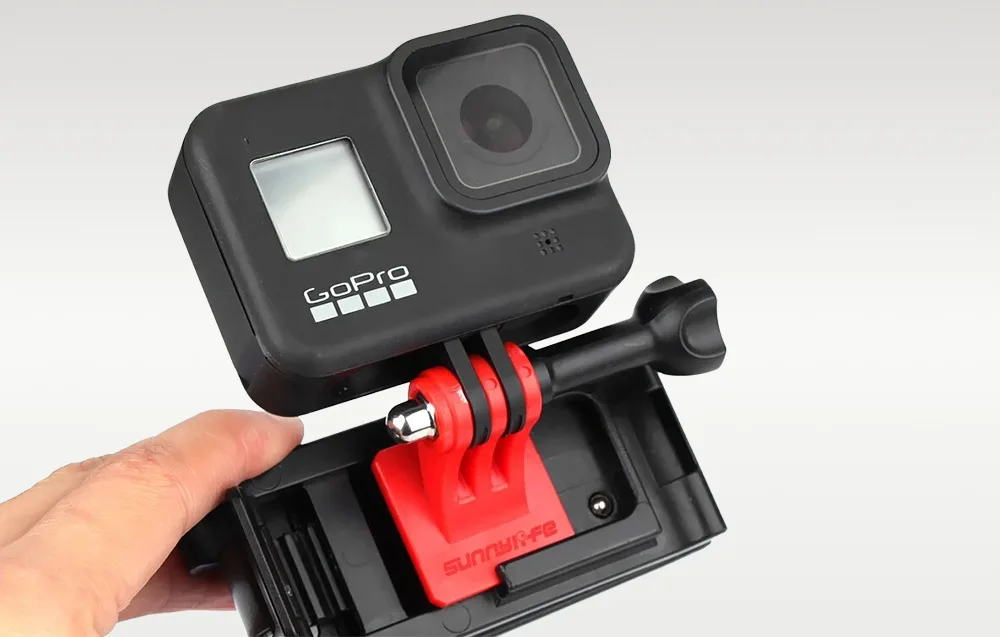 Рука тримає кліпсу з камерою GoPro, демонструючи спосіб кріплення на лямці рюкзака