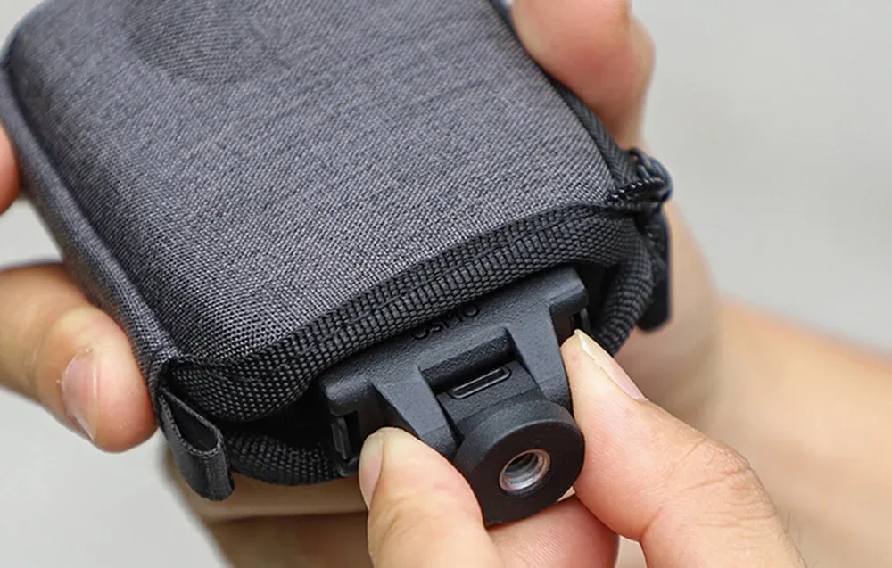 Hands holding a gray Sunnylife case for DJI Osmo 360 with a black mounting clip and USB-C port detail