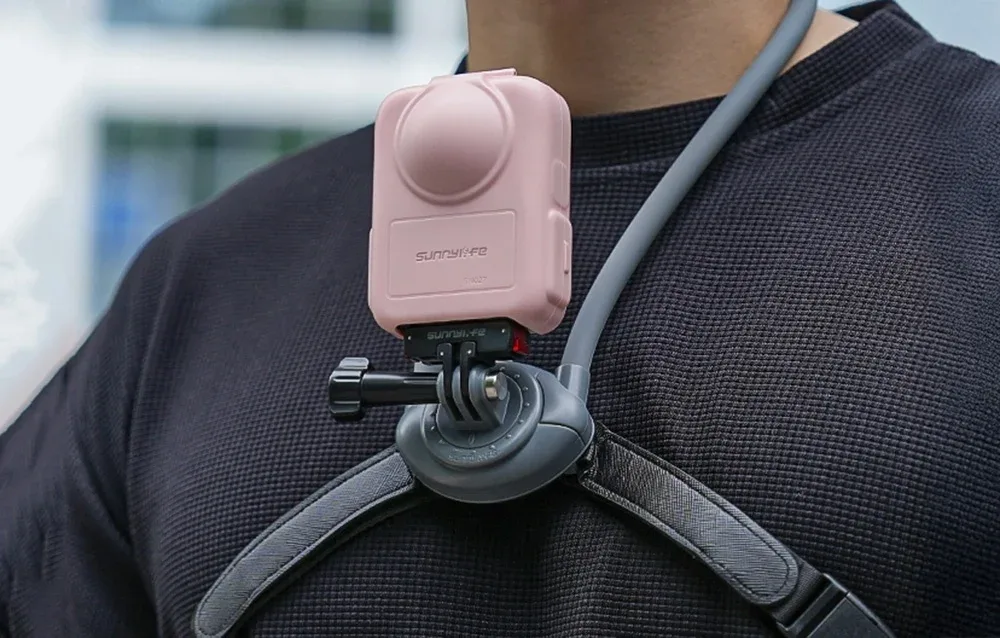 DJI Osmo 360 camera mounted on a chest harness in a pink Sunnylife protective case.