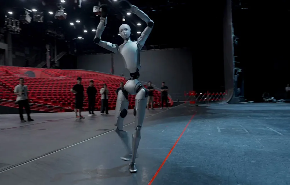 UNITREE H2 humanoid robot dancing on a stage in front of red cinema seats and an audience