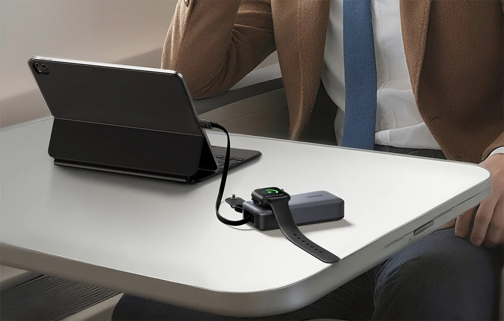 Man sitting at a table with a tablet connected to the power bank and a smartwatch nearby