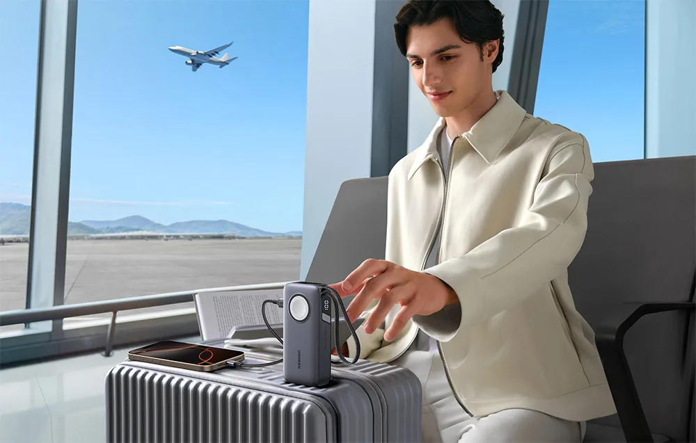Man sitting at the airport with a power bank connected to a smartphone on a suitcase
