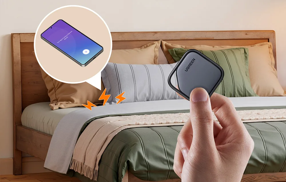 Локатор UGREEN у руці, на задньому плані смартфон на ліжку