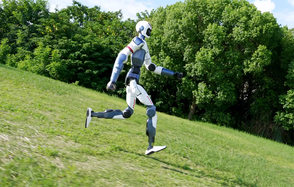 UNITREE R1 Basic humanoid robot running down a green hillside with trees in the background