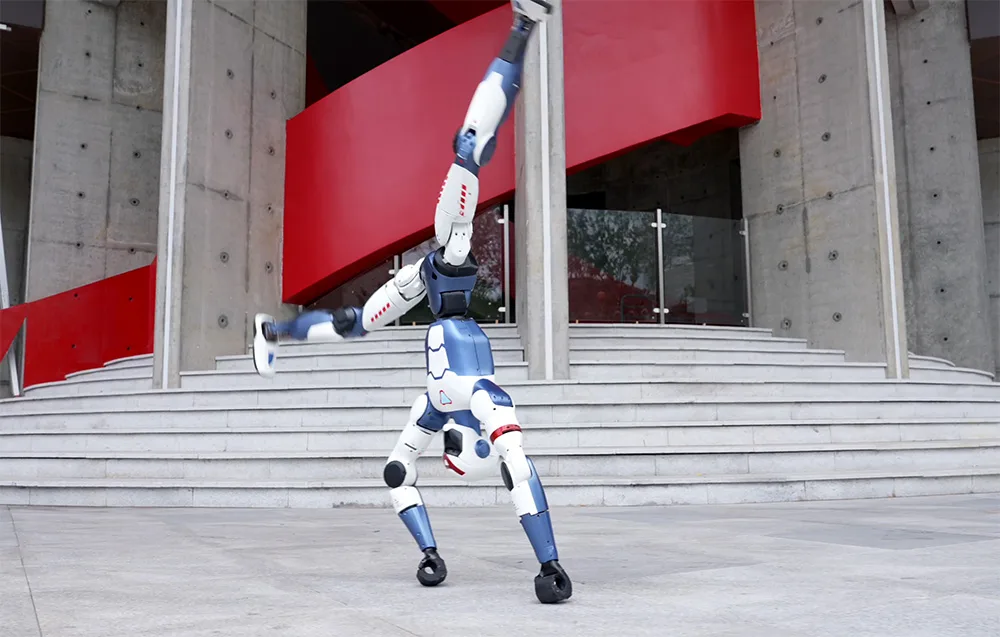 UNITREE R1 Basic humanoid robot performing a forward handspring in front of a modern building
