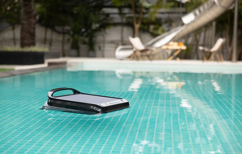 WYBOT F1 smart pool cleaning robot floating in a pool next to a terrace with loungers