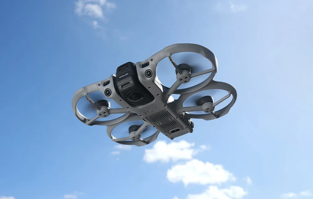 Вигляд знизу на дрон DJI Avata у польоті на тлі блакитного неба з білими хмарами