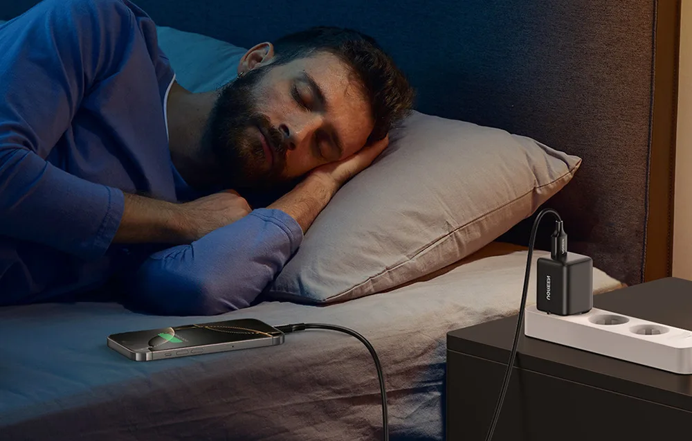 Smartphone connected to the Ugreen X518 charger beside a bed