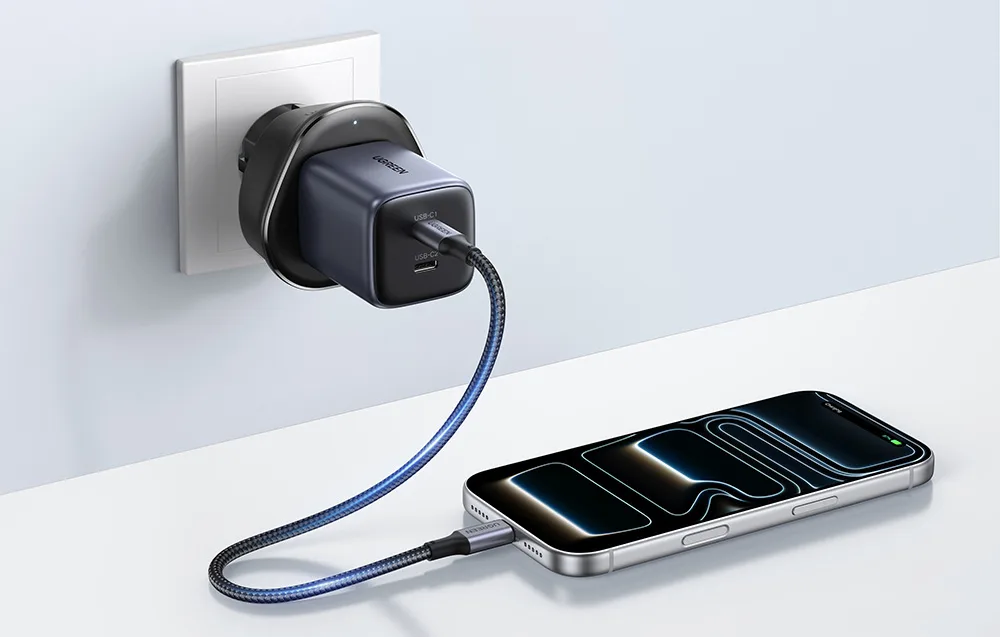 UGREEN S500 travel adapter plugged into a wall socket while charging a smartphone.