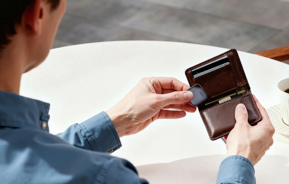 A person placing the UGREEN smart tracker into a leather wallet over a table.