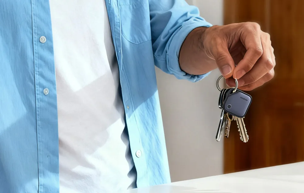 A person holding a set of keys with a UGREEN smart tracker attached.
