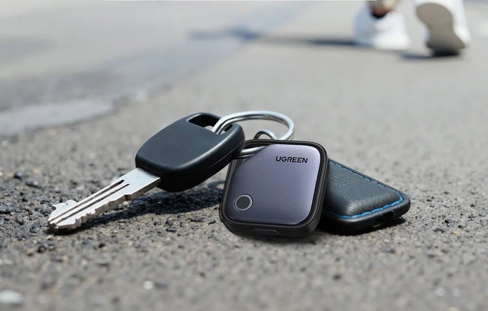 UGREEN smart tracker attached to a keychain with keys and a case placed on an asphalt road.