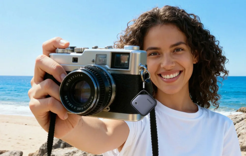 A woman on the beach holding a camera with a UGREEN smart tracker attached to the camera strap.